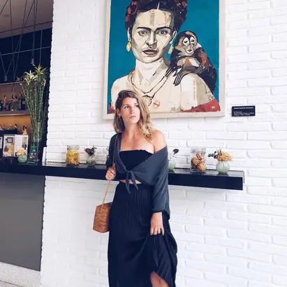 Donna in piedi di fronte a un ritratto di Frida Kahlo, mentre ammira l'iconica opera d'arte.