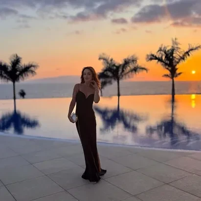Woman in an elegant black dress with the sunset and swimming pool in the background at H10 Atlantic Sunset.