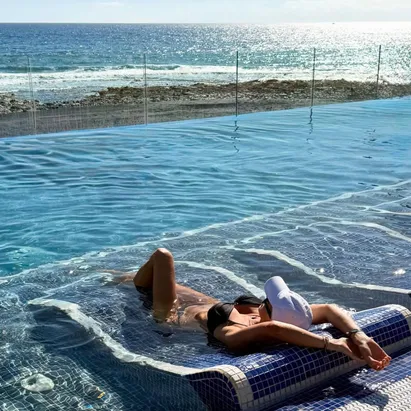 Mujer acostada en una esterilla de cerámica dentro de la piscina del H10 Costa Adeje Place, admirando el mar que queda justo en frente