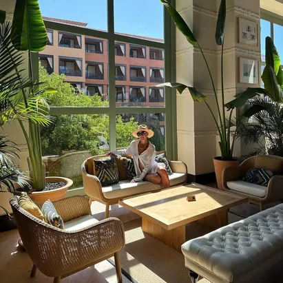 Mujer sentada en uno de los sofás del H10 Costa Adeje Palace, con un ventanal grande detrás y plantas alrededor