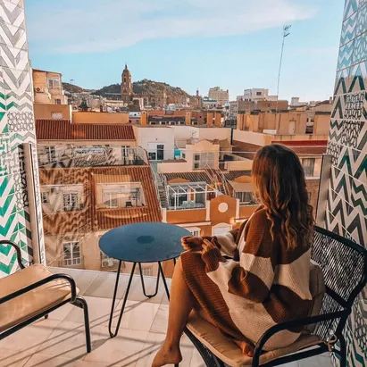 Donna con un maglione lavorato a maglia seduta sulla terrazza della sua camera all'H10 Croma Málaga, mentre guarda la città.