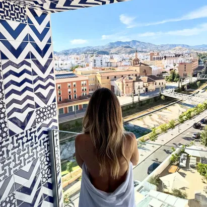 Donna in abbigliamento da ufficio sulla terrazza panoramica dell'H10 Croma Málaga al crepuscolo.
