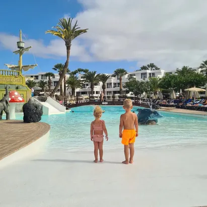 Niño y niña en la piscina de espalda mirando hacia la piscina de H10 Lanzarote Gardens
