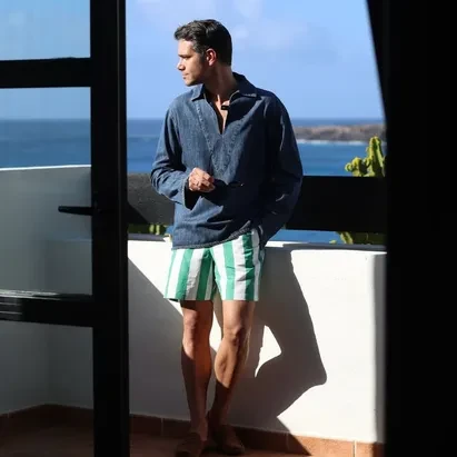 Man wearing a long-sleeved denim shirt and striped beach shorts on his room terrace with sea views at H10 Rubicón Palace.