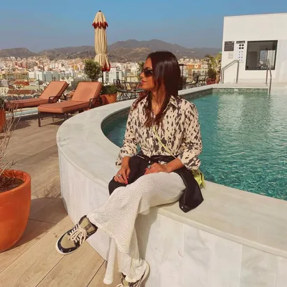Donna seduta a bordo piscina sulla terrazza panoramica dell'H10 Croma Málaga, con la terrazza e la vista sulla città di Málaga sullo sfondo.