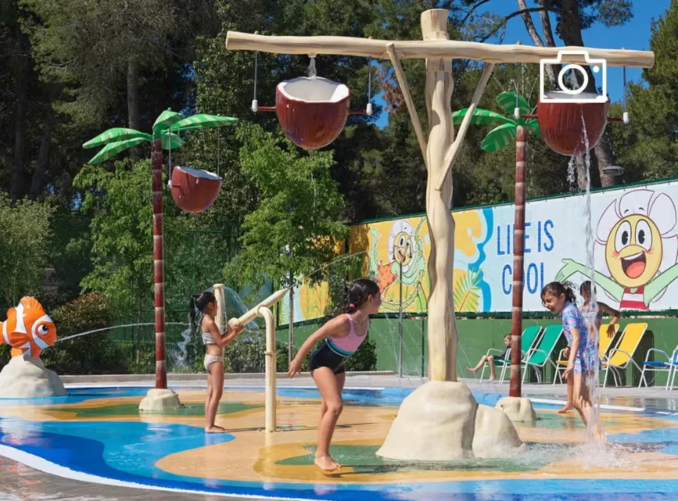 Niños jugando en los chorros de agua del Daisy Club en la piscina infantil de un hotel vacacional.